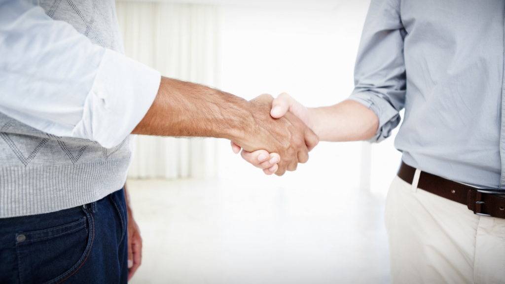 Two people shaking hands in a bright room, signaling agreement or partnership.